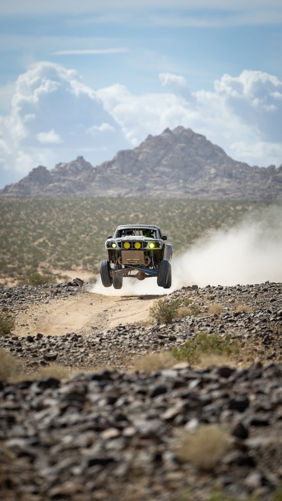 Ford Ranger race truck mid-air after launching off a jump on the desert race course, with a cloud of dust billowing behind it